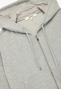 Lys grå zip-up hoodie med en glat tekstur, der har en kangaroo lomme, snore og en kontrasterende foring i hætten.