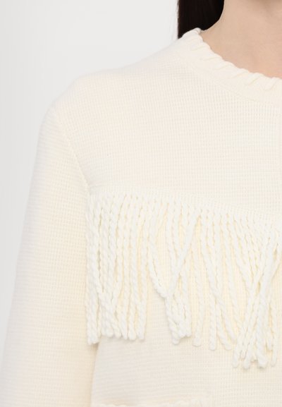 Cremfarbener Pullover mit strukturiertem Strick, der ein Fransenakzent in der Mittelpartie aufweist. Der geraffte Ausschnitt fügt eine subtile Detailverzierung hinzu.