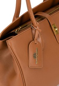 Sac à main en cuir marron avec une finition texturée, double poignées, fermeture éclair dorée et une étiquette de marque attachée.