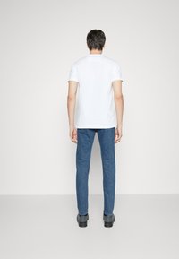 Vitt kortärmat t-shirt som matchas med blå jeans. T-shirten har en enkel design; jeansen har en texturerad yta och slim fit.