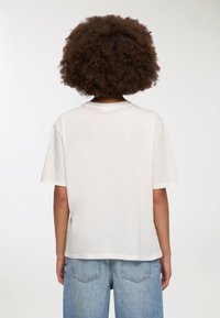 Biała bawełniana koszulka z krótkim rękawem, luźny krój, okrągły dekolt i gładka tekstura. Zestawiona z jasnoniebieskimi szortami dżinsowymi.