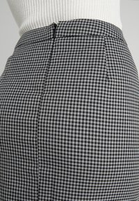 Close-up of a high-waist black-and-white houndstooth skirt with a side zipper worn with a white ribbed top.