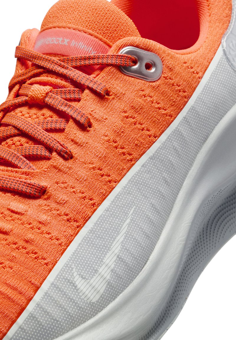 Jasnopomarańczowy but sportowy z teksturowanym cholewką, kontrastującymi sznurówkami, srebrnym okiem i białą podeszwą środkową z szarym logo Swoosh.