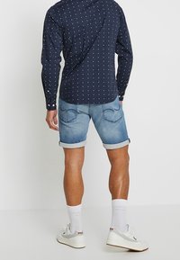 Granatowa koszula z guzikami, w małe białe kropki, połączona z jasnoniebieskimi szortami dżinsowymi, podwiniętymi na końcach. Białe trampki z logo i widocznymi skarpetkami.