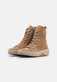 Tan suede high-top sneakers with textured rubber soles, featuring lace-up fronts, side zippers, and orange accents on the heel.