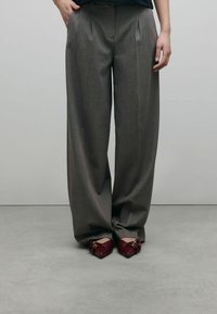Pantalons gris taille haute, à jambe large avec plis sur le devant. Associés à des chaussures rouges à bout pointu avec des accents floraux.