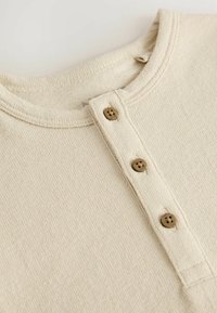 Chemise beige texturée avec encolure ronde, patte de boutonnage à trois boutons marron et tissu doux pour le confort.