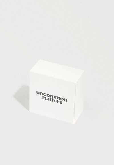 Valkoinen kuutiomainen laatikko, jossa on teksti “uncommon matters” lihavoidulla mustalla fontilla. Sileä pinta, selkeä muotoilu ja viistot reunat.