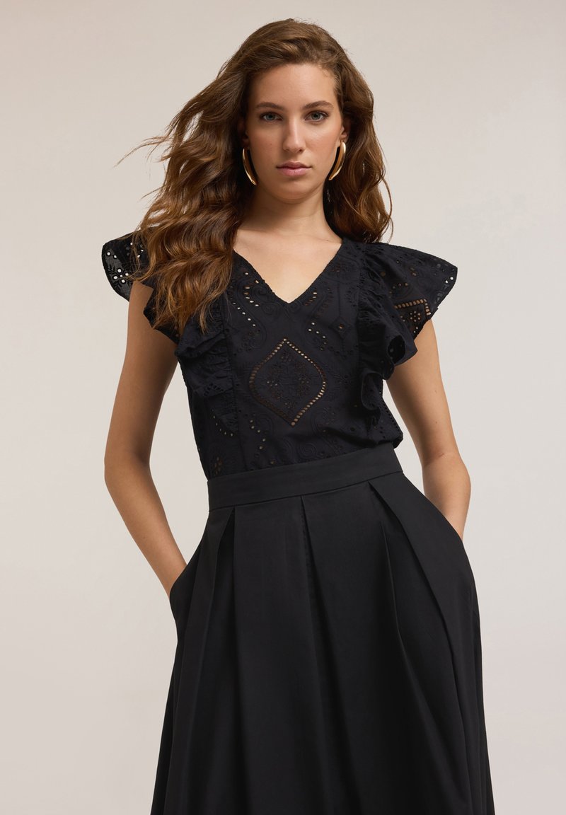 Blusa nera con maniche a sbuffo, con dettagli ad occhiello e scollatura a v, abbinata a una gonna nera plissettata con tasche.
