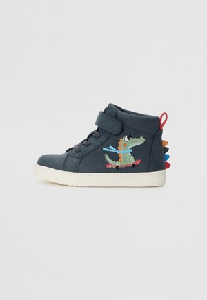 Shoe em cima do tornozelo de camurça azul com fita adesiva, apresentando um personagem de crocodilo verde em um skateboard e espinhos multicoloridos no calcanhar.