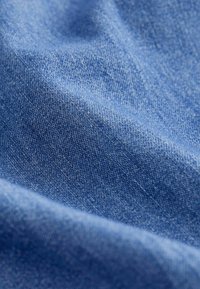 Gros plan sur un tissu bleu doux et texturé avec des motifs de tissage visibles et des plis délicats créant des ombres et des reflets.