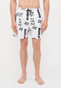 Pantaloni da bagno bianchi con un motivo astratto nero e grigio, cintura con cordino e lunghezza sopra il ginocchio. Realizzati in materiale leggero.