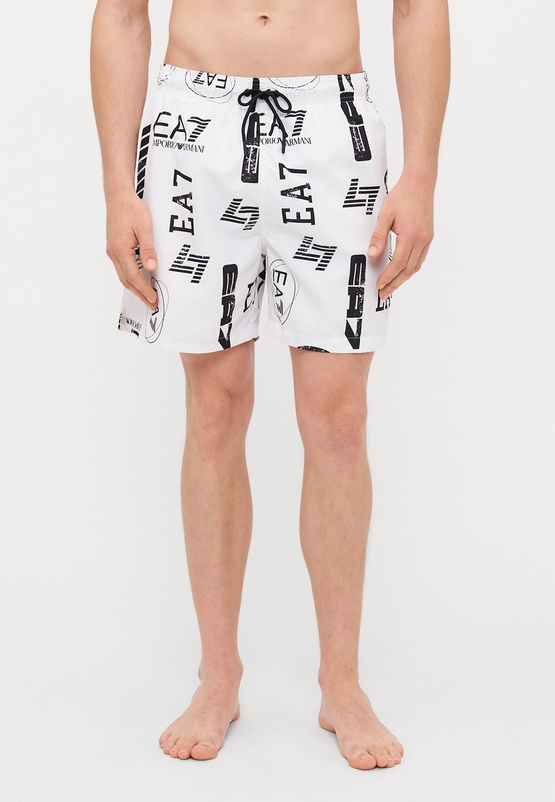 Pantaloni da bagno bianchi con un motivo astratto nero e grigio, cintura con cordino e lunghezza sopra il ginocchio. Realizzati in materiale leggero.