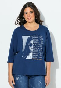 Granatowa koszulka z 3/4 rękawem z grafiką i tekstem w białym i pomarańczowym kolorze, przedstawiająca twarz kobiety w okularach przeciwsłonecznych. Miękki materiał.
