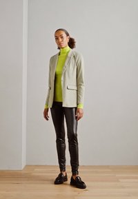Ljusgrå blazer, ljusgrön polotröja, svarta läderleggings och svarta loafers. Släta texturer och skräddarsydd passform. Enkelt designutseende.