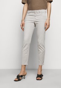 Jean gris clair coupe slim, cinq poches, avec un détail de surpiqûres discrètes, associé à des sandales à talons noires au design noué.