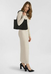 Zwarte leren tote bag met een gladde textuur en een reliëfpatroon, voorzien van twee korte handvatten en een rechthoekige vorm, vastgehouden door een persoon.