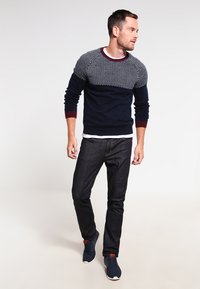 Navy and light blue patterned sweater with a solid dark bottom; paired with dark jeans and navy sneakers. Form-fitting design with ribbed cuffs.