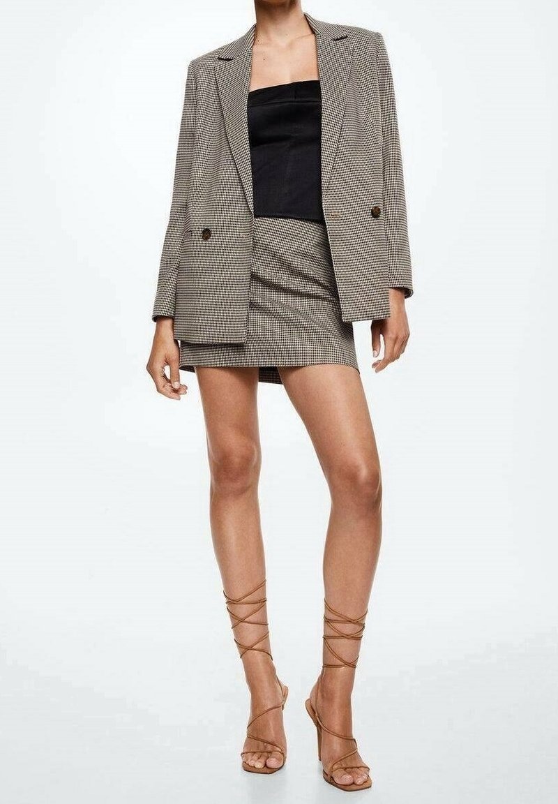 Tarkistusbleiseri beessissä ja mustassa, yhdistetty tiukkaan mustaan toppiin ja vastaavaan mini-hameeseen. Kirkkaat hihnalliset korkokengät viimeistelevät asun.