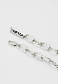 Catena in metallo argentato con link ovali, dotata di un'etichetta rettangolare incisa con "WFTW" e un gancio a un'estremità. Superficie liscia e riflettente.