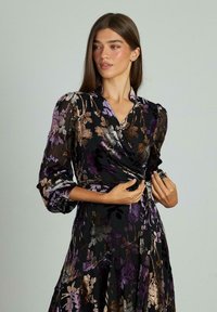 Vestido envolvente de manga larga en tejido negro translúcido con estampados florales en tonos púrpura, dorado y marrón. Con mangas fruncidas.