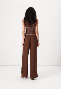 Brun smockad crop top i kombination med lösa, vida bruna byxor, som visar en mjuk textur och avslappnad passform.