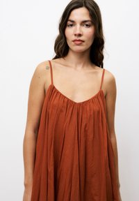 Terrakotta ärmelloses Kleid mit lockerer Passform, das einen gerafften Ausschnitt und dünne Träger hat. Hergestellt aus leichtem Stoff mit weicher Textur.
