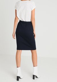 Jupe bleu marine côtelée longueur genou avec une silhouette ajustée, associée à une chemise blanche à manches courtes et des bottines blanches à talons blocs.