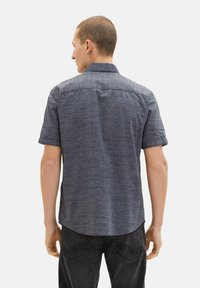 Kortärmad, marinblå skjorta med texturerad tyg, subtilt mönster, knäppkrage och böjd fåll, parat med mörka jeans.