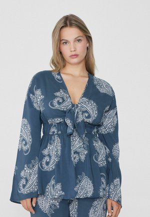 Marineblaue Bluse mit weißen Paisleymustern, V-Ausschnitt, Krawattenfront und langen Ärmeln. Glattes Material mit fließendem Design. Elastisches Taillendetail.