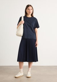 Navy t-shirt with a small logo, paired with a pleated navy skirt. Accessories include a light beige bag and white sneakers with gum soles.