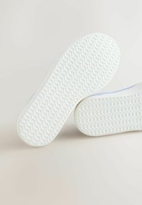Two white sneaker soles with textured hexagonal tread patterns on a light background, showing grip details.
