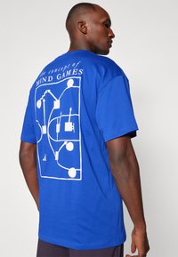 Blue cotton t-shirt featuring a large white graphic design on the back, including text and abstract shapes. Short sleeves and relaxed fit.