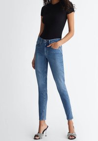 Jeans ajustados de mezclilla azul; cuentan con cinco bolsillos, una cintura estándar y un ligero desgaste. Combinados con una blusa negra de canalé y tacones.