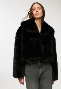 Czarna krótka kurtka z sztucznego futra z szerokim kołnierzem i długimi rękawami, zestawiona z szarymi jeansami o teksturze. Gładka, miękka faktura i błyszczące wykończenie.