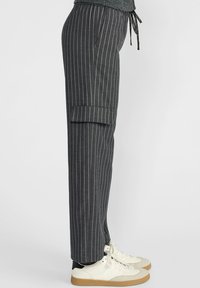 Vue de côté d'une personne portant un pantalon à rayures grises foncées avec ourlet et des baskets blanches à semelles en gomme.