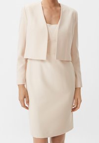 Ljusbeige klänning med figurnära siluett och en kort jacka med långa ärmar. Slät textur, minimalistisk design och inga synliga mönster.