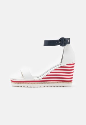 Sandalia de cuña blanca con una suela a rayas rojas y blancas. Presenta un diseño de punta descubierta, tira para el tobillo y detalles de yute en la cuña.