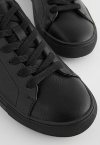 Svarta lädersneakers med strukturerad ovandel, rund tå och platt gummisula. Har svarta snören och subtila sömdetaljer.