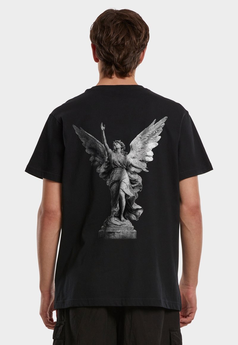 Moški v črni majici z detajlnim tiskom sivega kipa angela na hrbtu, ki prikazuje razprta krila in eno dvignjeno roko.
