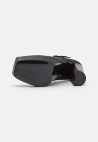 Czarny wysoki obcas z gładkiej skórzanej cholewki, prostokątnym kształcie noska i teksturowanej podeszwie dla lepszej przyczepności. Posiada subtelny akcent kokardy.