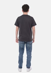 T-shirt in cotone grigio scuro con maniche corte, scollo tondo e taglio dritto, abbinata a jeans azzurri chiari e sneaker bianche.