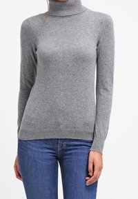 Grå polotröja gjord av mjukt stickat tyg. Formsydd design med långa ärmar och ribbade kanter. Bärs med blå jeans.