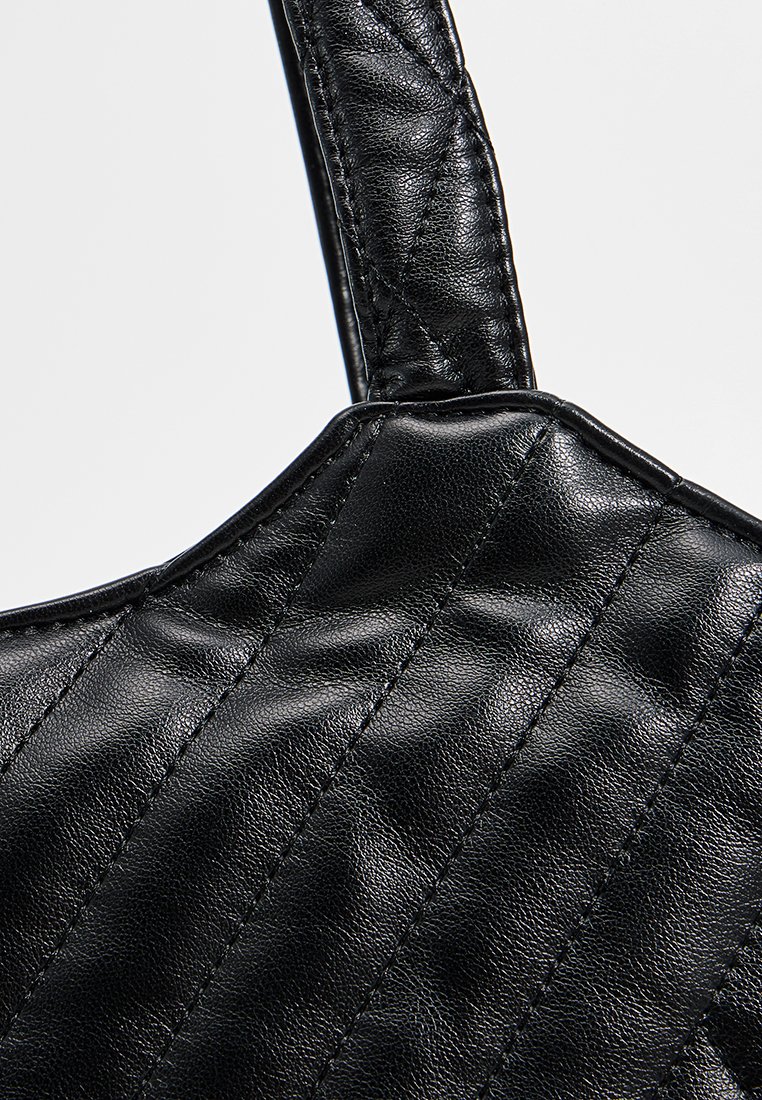 Sac en cuir noir avec un design texturé et matelassé et une bandoulière robuste. Présente des coutures visibles et une finition brillante.