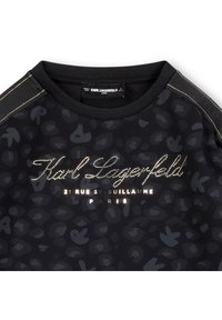 Svart genser med subtilt leopardmønster, ribbet rund hals og logotrykk med metalliske aksenter på brystet og skuldrene.