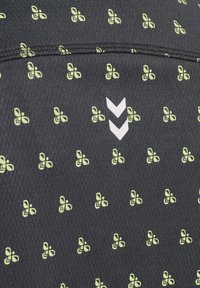 Svart tyg med ett upprepat mönster av gula fjärilar och en vit chevronlogotyp. Mjukt i texturen och med sydda kanter.