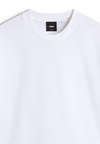 Hvid t-shirt med korte ærmer lavet af bomuld. Har en rund halsudskæring og en lille sort label med "VANS" og størrelse "MELLEM" nær halsen.