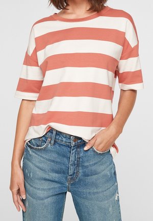 Gestreiftes T-Shirt in Terrakotta und Creme. Kurze Ärmel, runder Halsausschnitt, weiches Baumwollmaterial. Kombiniert mit verwaschenen blauen Jeans.