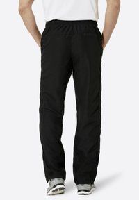 Schwarze Sporthosen mit einem elastischen Bund, ausgestattet mit Seitentaschen und einer schmal zulaufenden Passform. Getragen mit grauen Sportschuhen.