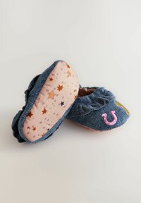 Zapatillas de denim con un borde rizado, que cuentan con un bordado de herradura rosa y un diseño amarillo. Suelas rosas con un patrón de estrellas y puntos.